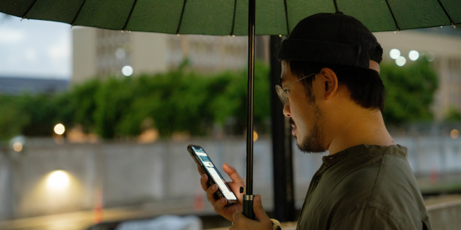 A man holding an umbrella while looking at his phone.