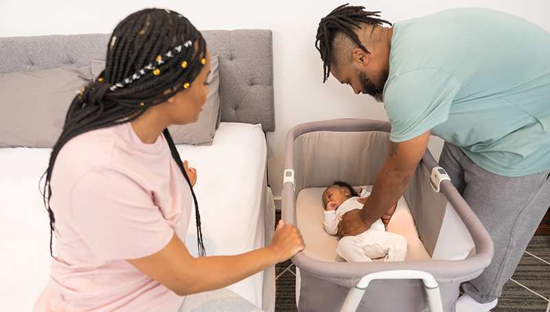 A mother and father placing their child in a crib. 