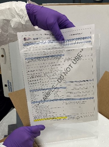 A person in a protective suit wearing gloves places a submission form