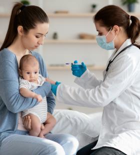A young mother holds an infant while a doctor gives the baby a vaccine