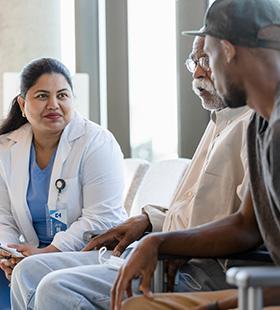 A female doctor sits with an elderly patient and family caregiver