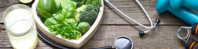 Salad in a heart-shaped bowl, glass of water, a stethoscope, and hand weights on a table.